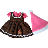 An 18-inch doll dress in brown with a small repeating pattern, pink ruffled sleeves, white scalloped trim, and a gingerbread man appliqué, shown next to a pink Santa hat with a white pom-pom.