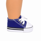 A royal blue canvas tennis shoe sneaker with white laces, a white rubber toe cap, and a black and white sole, shown on an 18" doll's leg.