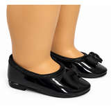 Black patent leather ballet flats with black ribbon bows and trim, shown on an 18-inch doll's legs against a white background.