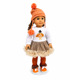 An 18-inch doll wearing a fall-themed outfit consisting of an orange knit pom-pom beanie, a white long-sleeve shirt with a turkey graphic, a brown skirt with a beige ruffled trim, and brown and orange striped tights.